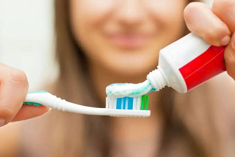 A person squeezing toothpaste from a tube onto a toothbrush.